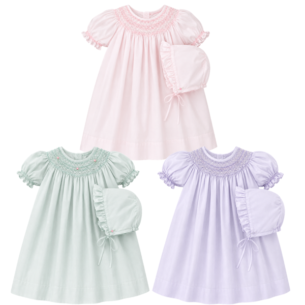 Three baby dresses in pink, mint, and purple with smocked details on a white background.