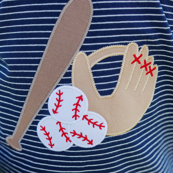 Close-up of a navy blue shirt with beige baseball glove, bat, and ball embroidery.