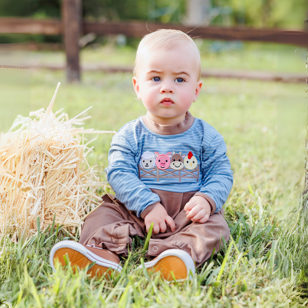 baby wearing farm animals romper sitting in a field