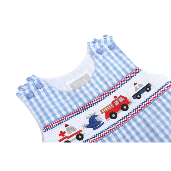 Close-up of smocking detail on blue gingham overalls, showing embroidery of ambulance, helicopter, fire truck, and police car.