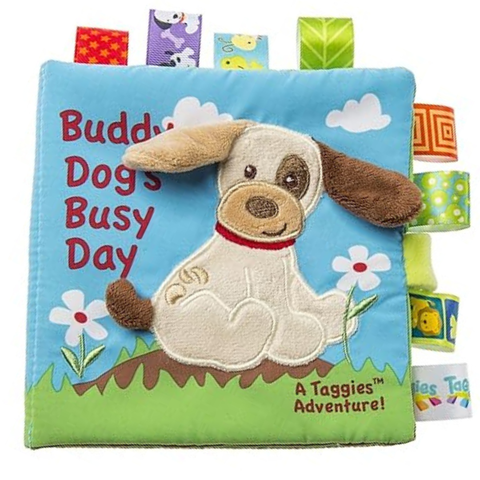 Children's soft book titled 'Buddy Dog's Busy Day' with a cartoon dog on a blue background and loops of tags along the edge