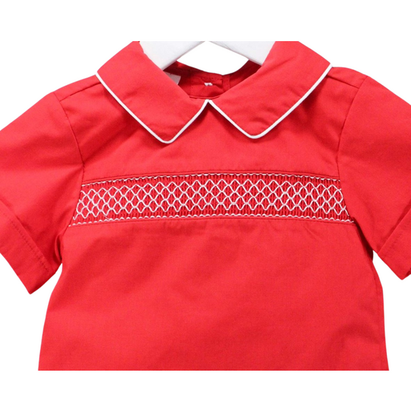Close-up of smocked chest detail with white threadwork and piped collar on red fabric.