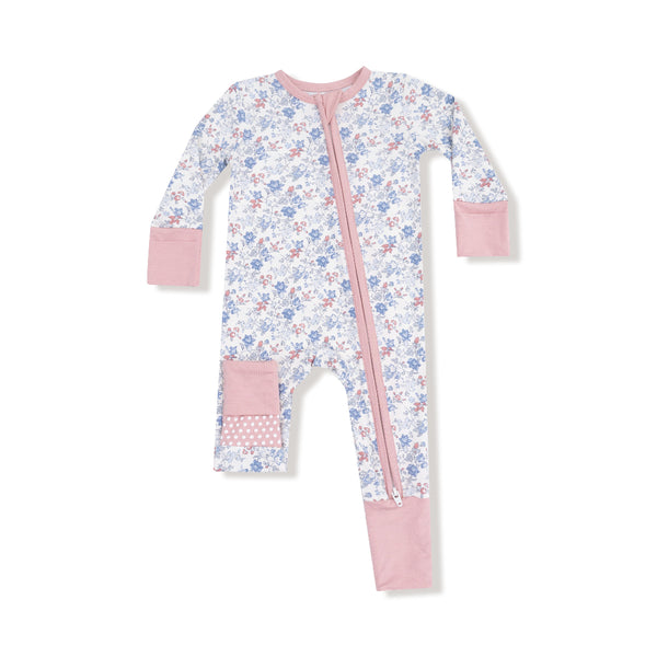 Baby romper with vintage floral print in blue and rose, pink trim, two-way zipper, and polka dot knee and footie accents.

