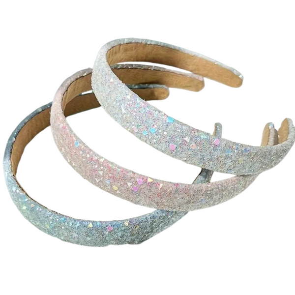 A product image showing three elegant, sparkling headbands stacked on top of each other. The headbands are covered in iridescent glitter in white, soft pink, and light blue, and are placed on a white background.