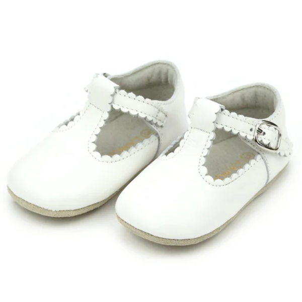 White scalloped baby mary jane crib shoe with soft sole and adjustable buckle strap.