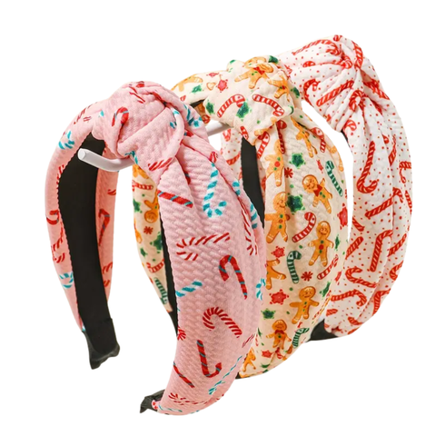Three padded knotted headbands, each with a different Christmas-themed pattern. From front to back: pink with red and blue candy canes, cream with gingerbread men and candy canes, and white with red candy cane dots.