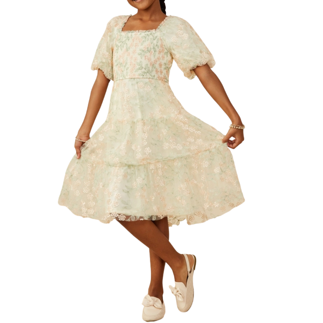 Girl wearing an ivory and mint lace dress with puff sleeves, smocked bodice, and tiered skirt, styled with bow flats.