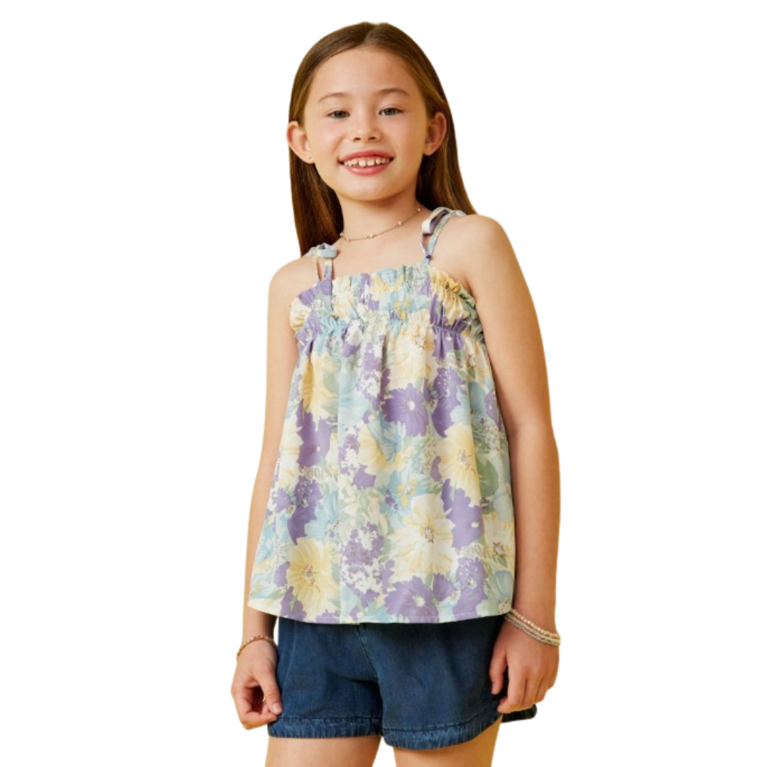 Girl wearing a soft floral print tank top with ruffle neckline and adjustable tie straps, paired with denim shorts.