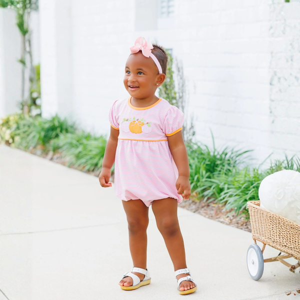 little girl wearing the pink and white stripe bubble trimmed in orange with triple pumpkin applique