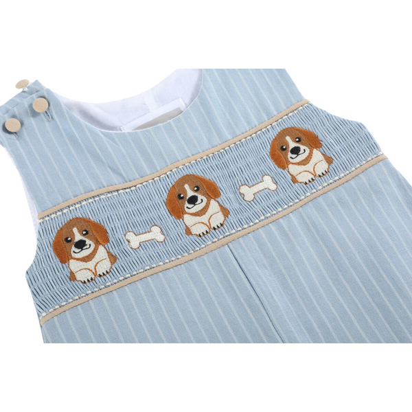 Close-up of smocking detail on blue pinstripe overalls showing three embroidered puppies and small white bones across the chest.