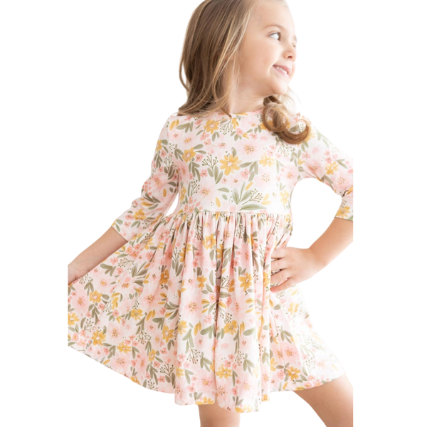 Girl wearing a blush floral long sleeve twirl dress while holding a pink handbag, featuring yellow and sage watercolor flowers.