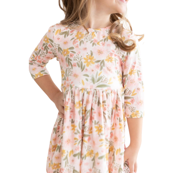 Close-up of a girl's blush floral dress with three-quarter sleeves, empire waist, and soft yellow and sage botanical print.
