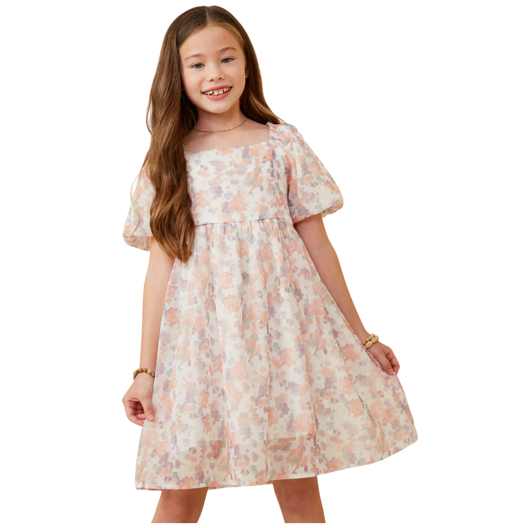 Girl wearing a pastel watercolor floral dress with puff sleeves, a square neckline, and a flared trumpet-style skirt.