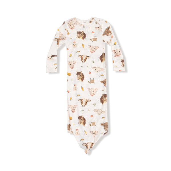 Knotted baby gown with vintage-style farm animals including pigs, cows, and horses on a soft white ribbed background.
