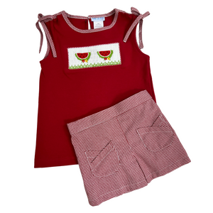 Red knit girls top trimmed at the neck and armholes in a red check gingham and ties at the shoulder.  Smocked center with watermelon and flowers. Matching red gingham shorts with two front criss crossed pockets