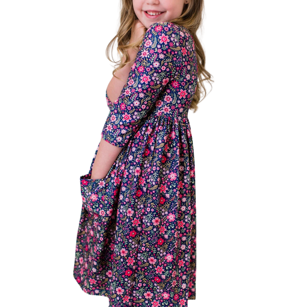 Side view of a girl's navy floral dress featuring three-quarter sleeves, hidden side pockets, and a full gathered skirt.